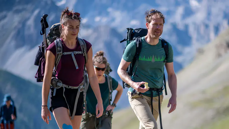 Drie bergwandelaars die met rugzakken over een bergpad wandelen.